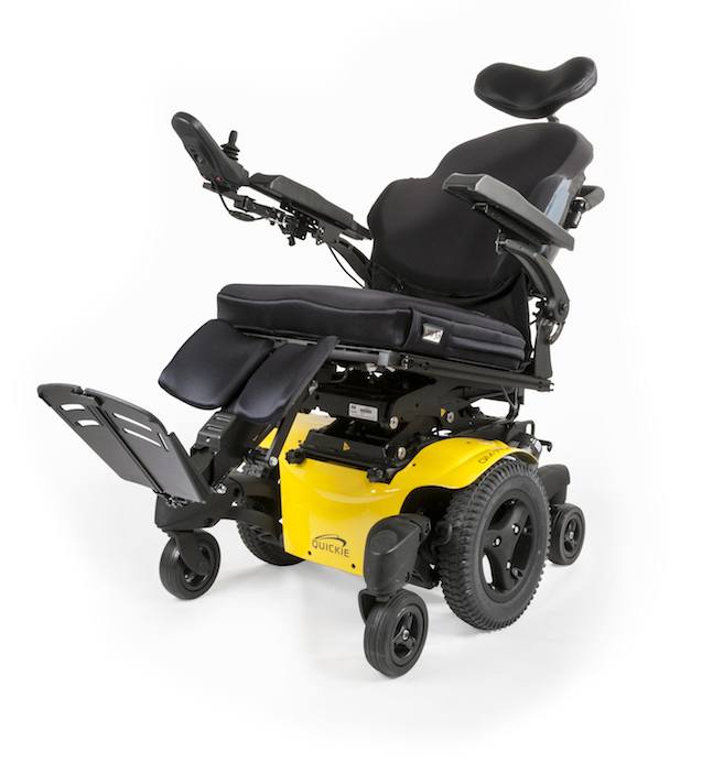 The image shows a bright yellow and black powered wheelchair with an adjustable, contoured black seat and headrest. It features armrests and has a joystick control mounted on the left side. The chair also has elevating leg rests and footplates. It appears to be a model designed with tilt and recline functionality, consistent with a power wheelchair.