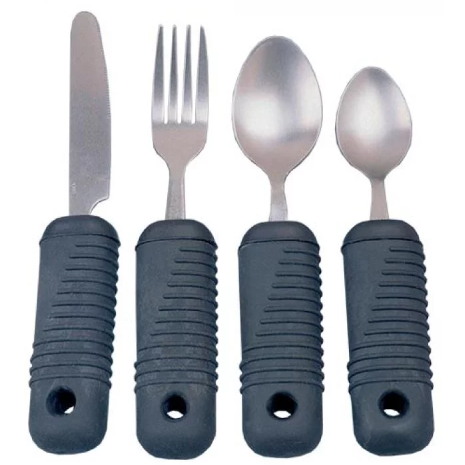 The image shows a set of four stainless steel weighted eating utensils: a knife, a fork, a tablespoon, and a teaspoon. Each utensil has a thick, ribbed, black, non-slip rubber handle. The handles are designed for an easy and secure grip and appear to have a hole near the bottom. These types of utensils are often used to assist people with hand tremors or limited grip strength.